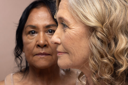Diverse female friends with senior posing closely in studio on beige backdrop in thin-strap tops