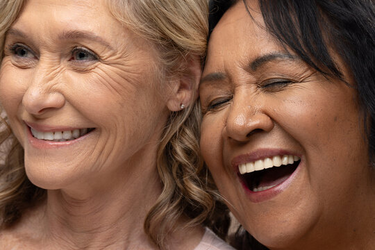 Senior and mature female friends smiling and laughing in studio showing stud earring pink dark tops