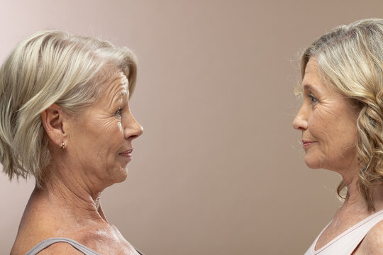 Senior women facing each other with beige backdrop and soft lighting, wearing thin straps