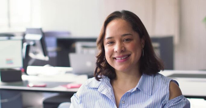 African American woman smiling and fixing blouse cutout replying to camera cue by monitor in office