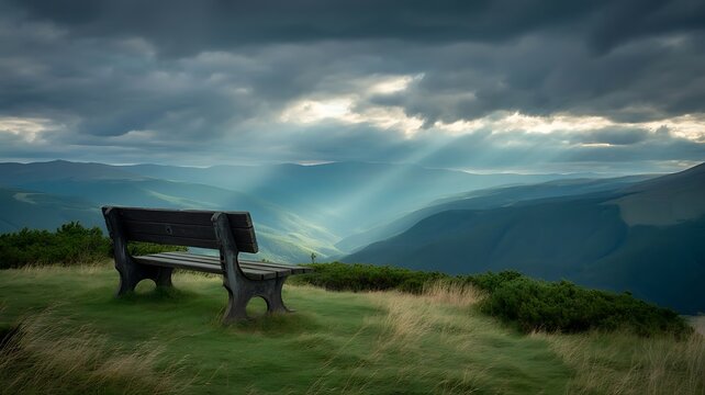 Wooden bench on a grassy hill overlooking a vast mountain range under a dramatic cloudy sky with sun rays breaking through the dark clouds