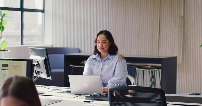 African American woman in blue blouse facing laptop, typing while working at desk in open office