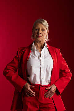 Senior woman posing in studio with red backdrop wearing red suit white shirt gold necklace
