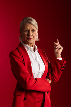 Senior female posing waist up in studio wearing red tailored blazer and pointing index finger