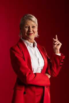 Senior female wearing red tailored suit with white shirt posing in studio, showing drop earrings