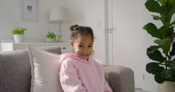 African American child in pink hoodie at home shifting gaze, smiling, laughing at person on right