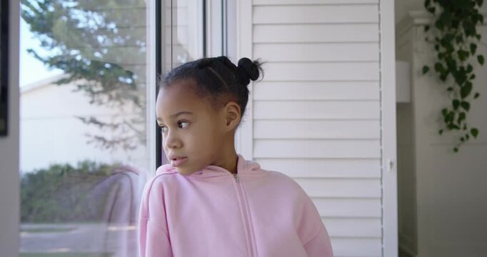African American child leaning at porch door watching yard, turning, smiling, showing missing tooth
