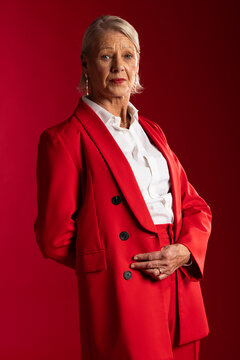 Senior female posing in studio wearing red double-breasted blazer, white blouse, gold earrings