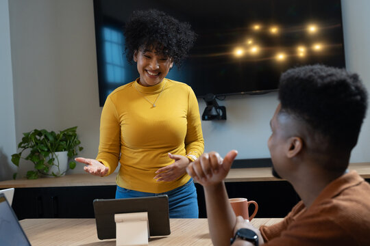 African American coworkers watching standing woman in yellow top presenting with tablet in office
