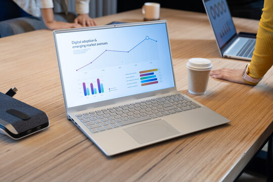 African American adult women reviewing charts on silver laptop at office table with USB stick