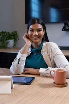 African American woman sitting at wooden conference table leaning on left hand smiling with tablet
