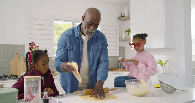 African American family at island, mature man teaching children leaning in, rolling dough with pin