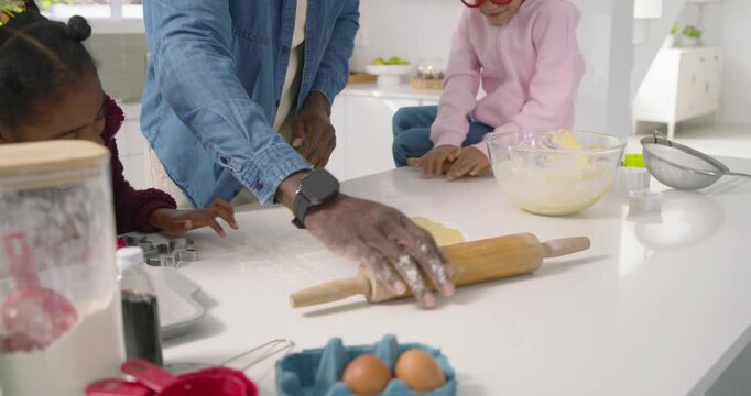 African American family watching dad placing and rolling dough with pin, folding in kitchen baking