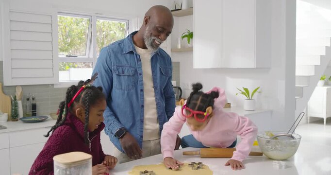Mature man placing metal cutters and pressing dough for cutting cookies, guiding youth girls