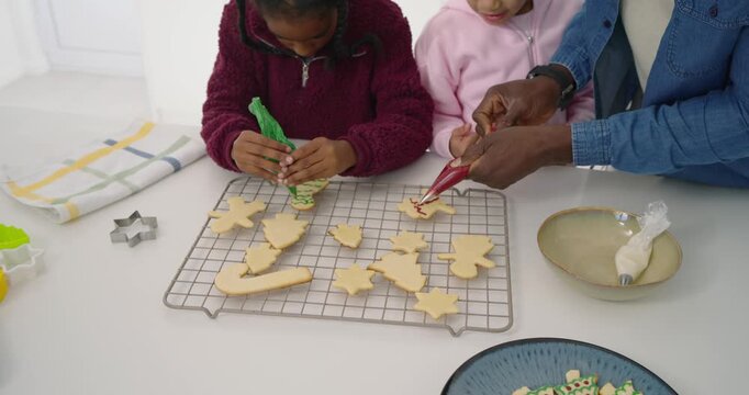 African American dad and girls decorating fresh cookies on rack squeezing green, red piping bags