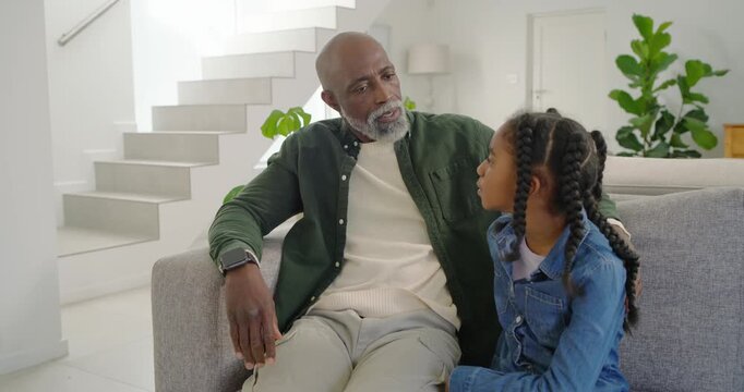 African American dad and child sitting on gray sofa at home, child appearing upset, dad comforting