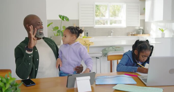African father with children raising fingers, teaching at table while older child writing on laptop