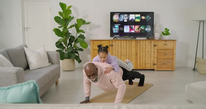 African American man and child exercising on tan yoga mat while child jumping onto back, bonding