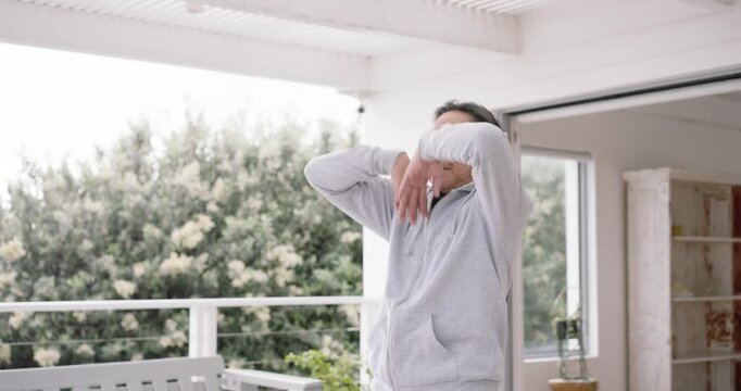 Senior Asian man doing repeated arm raises for calm on covered balcony by railing after inhale