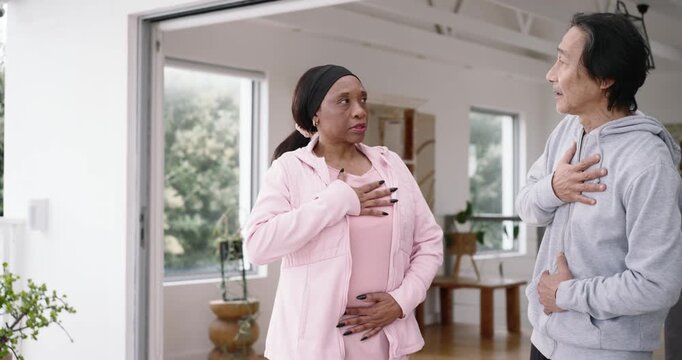 Senior man guiding pregnant woman through breathing for birth in living room, lavalier visible