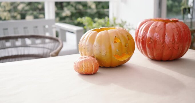 Camera is panning right on porch to reveal red pumpkin and lit jack-o'-lantern on table