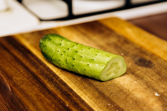 Fresh sliced cucumber on wooden cutting board close up, green vegetable prepared for cooking in kitchen, healthy food ingredient on rustic wood surface.