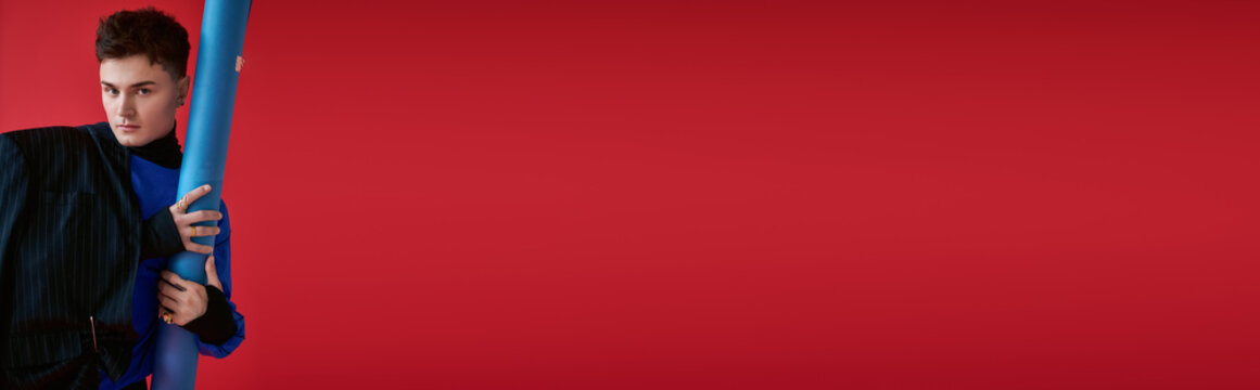Stylish young man in chic attire striking a pose against a vibrant red background
