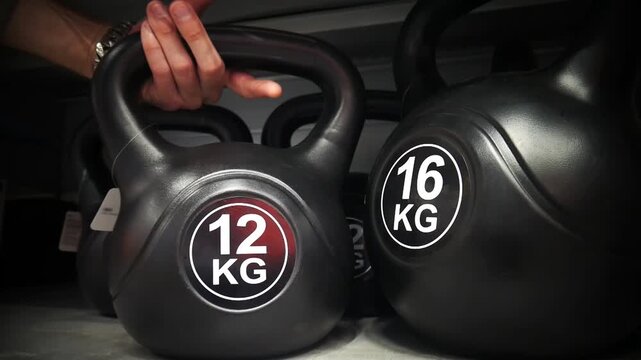 Close-up of a male customer's hand grabbing a 12 kg kettlebell from a sporting goods store shelf. Fitness equipment shopping concept
