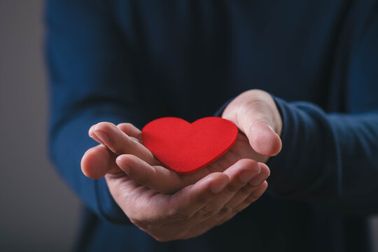 Hands holding a red heart symbolizing love, care, compassion, kindness, support, charity, donation, emotional connection, community, healthcare, social responsibility, and human connection.