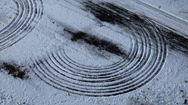 Elegant photo of Aerial view of dark tire skid marks forming circular patterns on fresh white snow. This image represents dangerous winter driving conditions and reckless behavior.