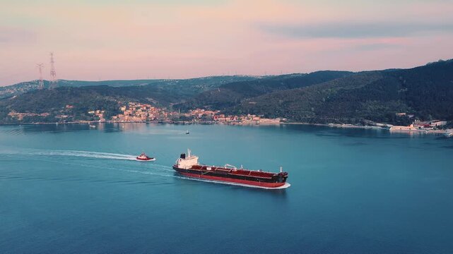 Aerial view of a large tanker vessel accompanied by a pilot boat navigating through calm waters in the soft light of early morning, representing global maritime trade and shipping logistics.