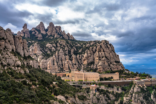 Stunning view of Santa Maria de Montserrat Monastery located under round rocky Montserrat Mountain in spring, Monistrol de Montserrat, Catalonia, Spain