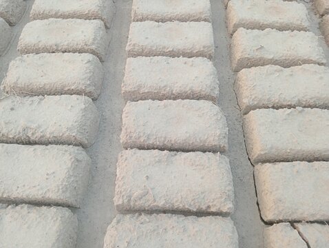 Mud brick production process photo. Handmade clay blocks drying in rows on ground outdoors. Traditional construction materials and masonry industry photography context.