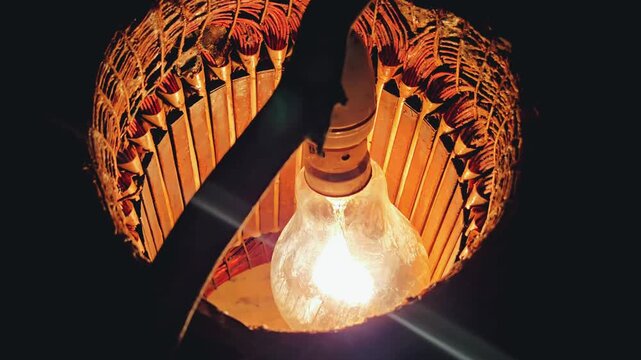 An incandescent tungsten bulb glows inside a water pump motor to dry out wet copper coils, captures a stark visual symbol of agrarian survival & rural infrastructure vulnerabilities after river floods