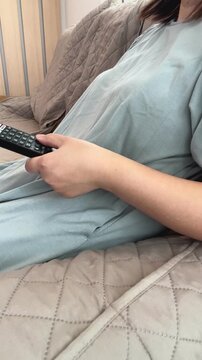 ソファーでくつろぎながらテレビのリモコン操作する女性