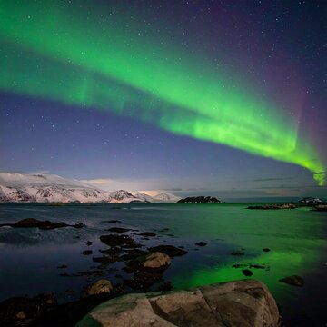 Green aurora borealis over snowy coast with rocks and starry sky