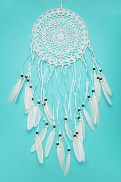 Handmade dream catcher hanging on a rope with feathers, threads, and beads on blue background.
