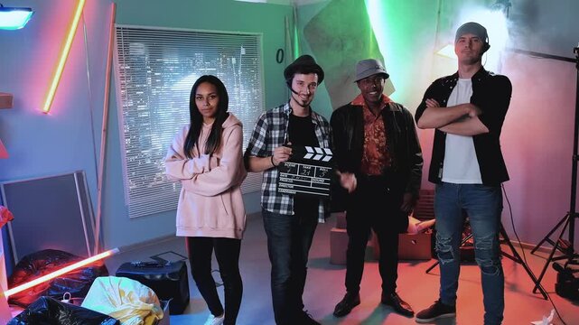 Five people on a professional indoor film set holding clapperboards and standing together under dramatic lighting during nighttime production.