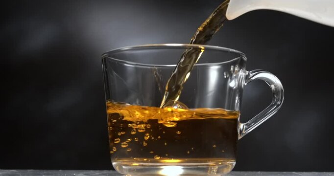 Tea pouring from teapot into transparent mug in slow motion