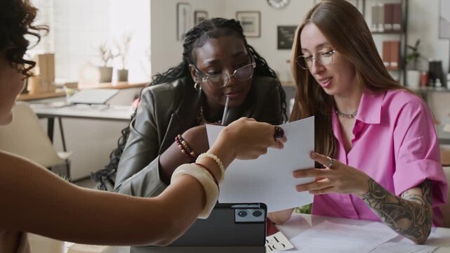 Multiethnic group of young adult female colleagues discussing graphic design layouts at meeting in office. Footage suited for corporate presentations or advertising agency promotional videos