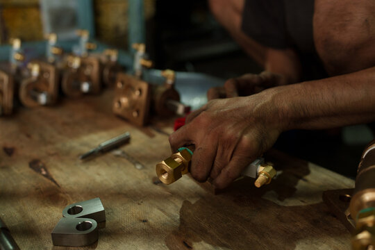 Focus on hands and machined brass metal parts in an industrial factory.