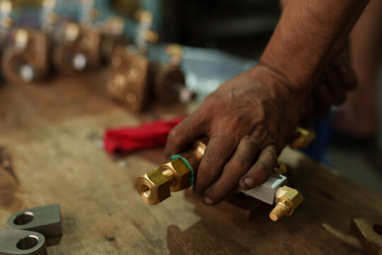 Focus on hands and machined brass metal parts in an industrial factory.
