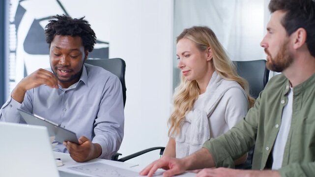Three diversity business managers in company coworking discuss papers analyzing startup statistic Caucasian businesswoman and businessmen talking looking in document talk work planning office project