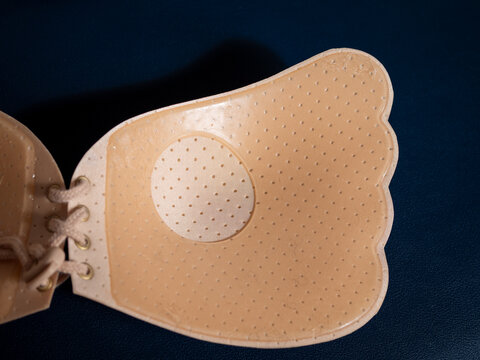 Close-up of the inside of a beige strapless adhesive bra with perforated cups and lace-up closure, designed to adhere to the body for discreet support under clothing.