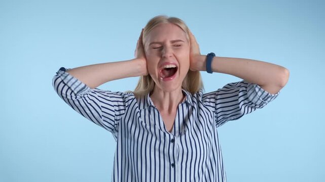A blonde woman wearing a striped shirt screams and covers her ears in distress against a solid blue studio background. Medium shot at eye level.