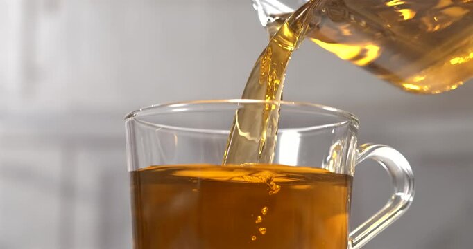 Tea pouring from glass teapot into transparent cup in slow motion
