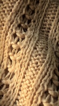 Close up of beige knitted wool sweater texture. Candid camera pan shot along warm fabric weave, soft yarn details, and cozy pattern for autumn and winter concepts.