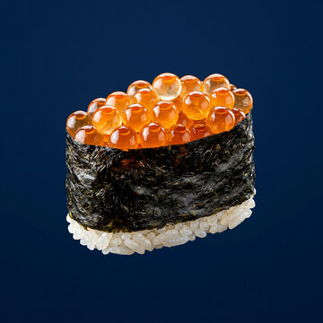 Single piece of Ikura gunkan sushi with salmon roe on a dark blue background.