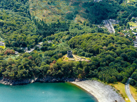 Aerial view of Dolbadarn Castle in Llanberis, Snowdonia, Wales, medieval stone tower standing on grassy hill surrounded by lush green woodland