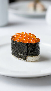 A single piece of ikura gunkan sushi on a white plate.